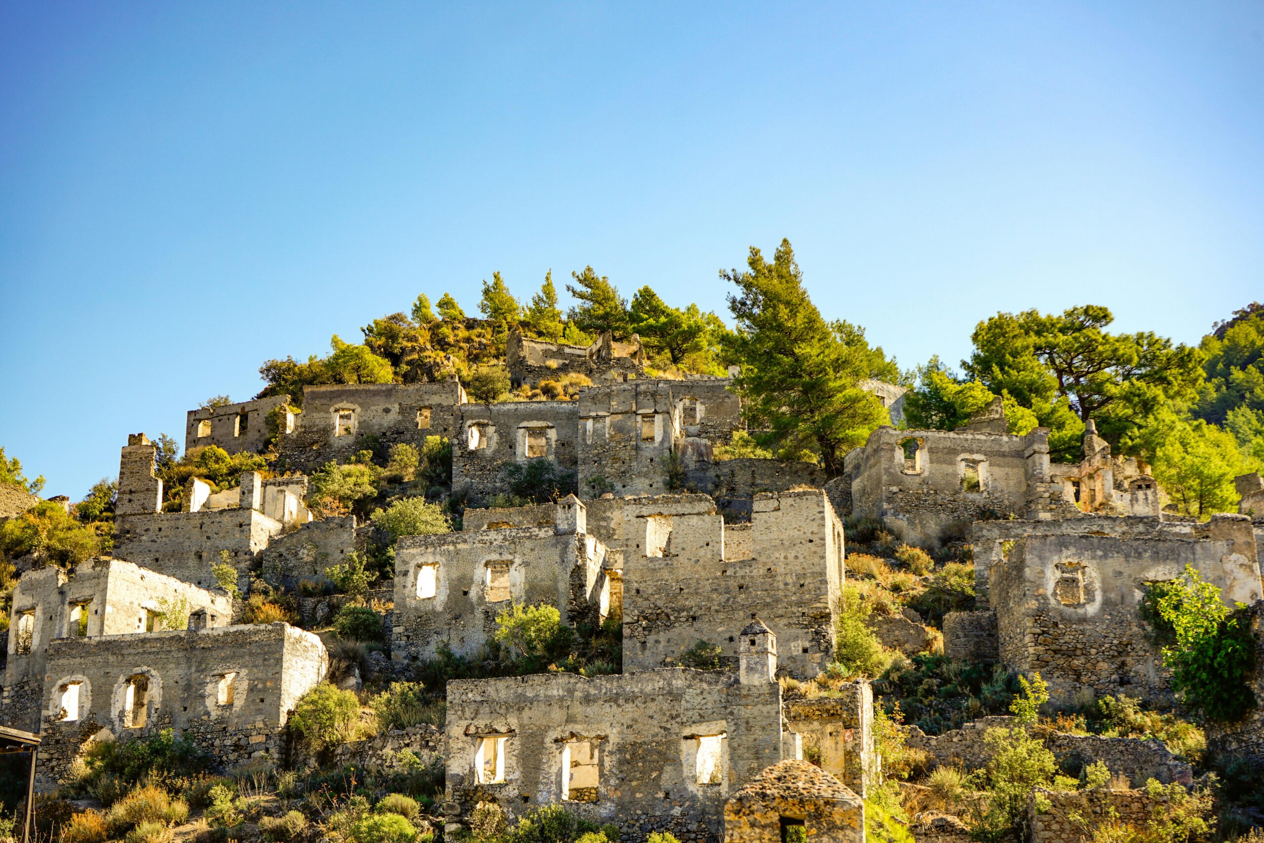 Discover the haunting beauty of Kayaköy ruins in Türkiye, set against a bright blue sky.