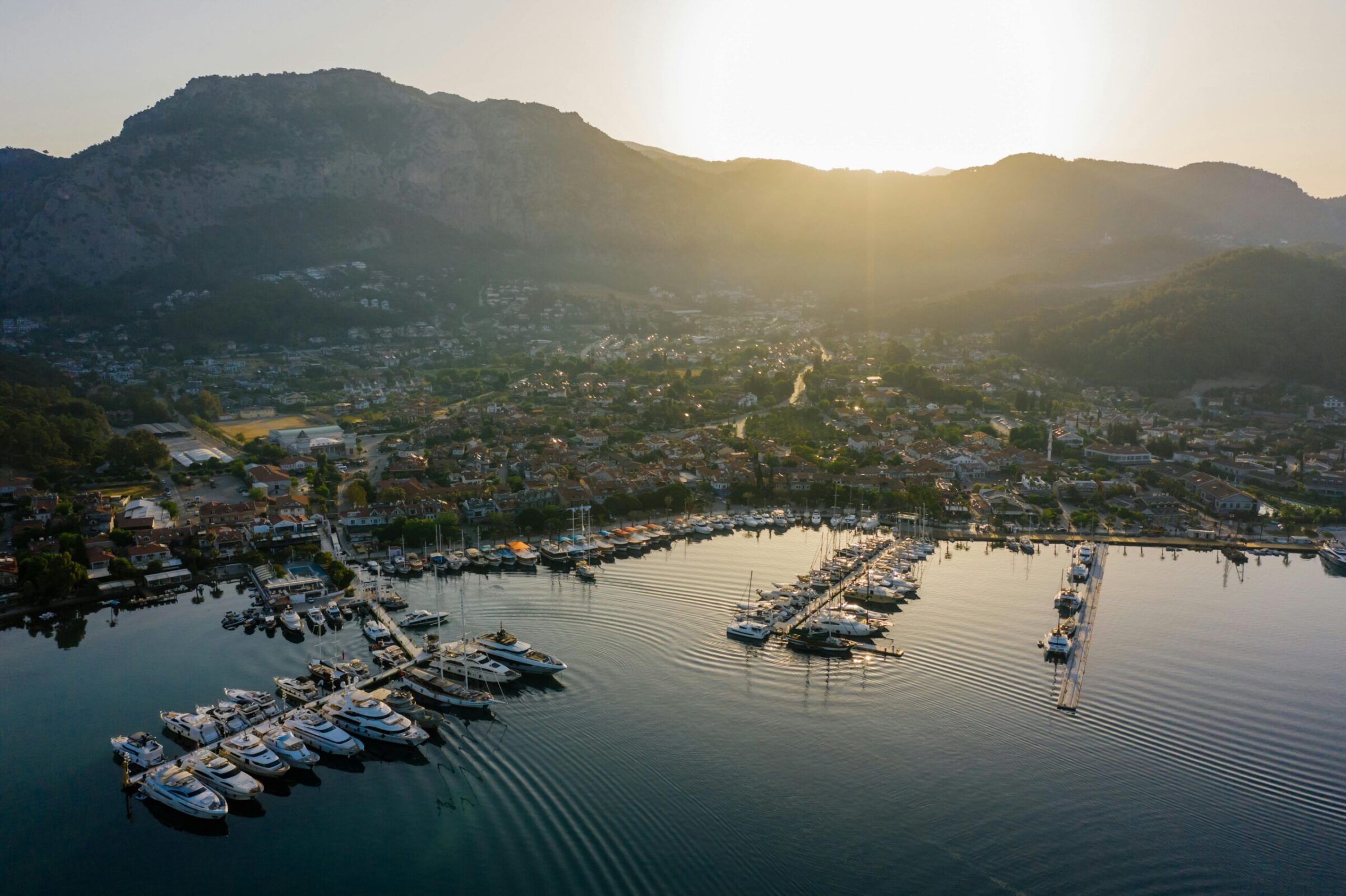 Drone view of a serene marina with boats against a mountainous backdrop during sunset.