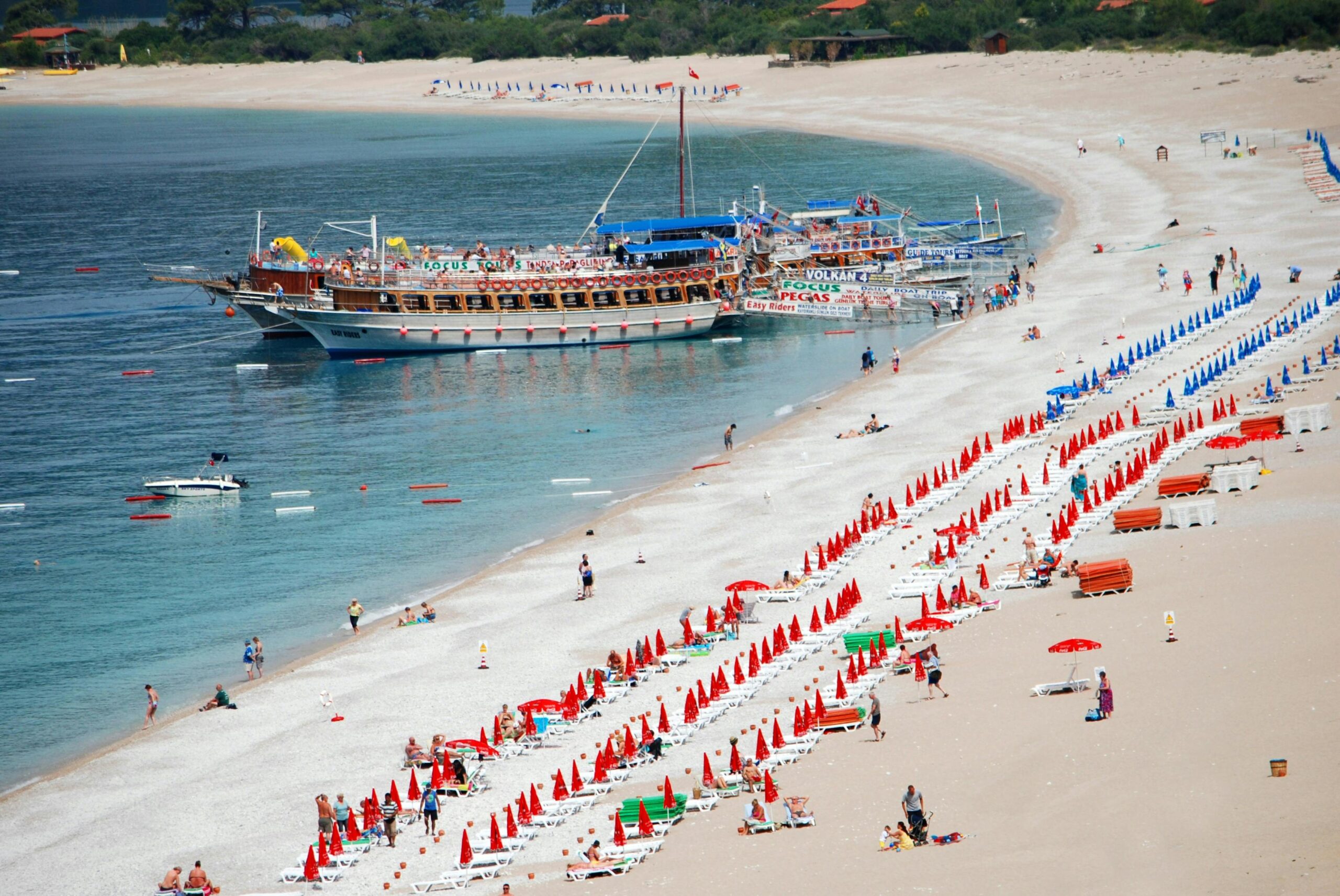 Vibrant beach scene in Fethiye, Türkiye with colorful umbrellas and boats on a sunny day.